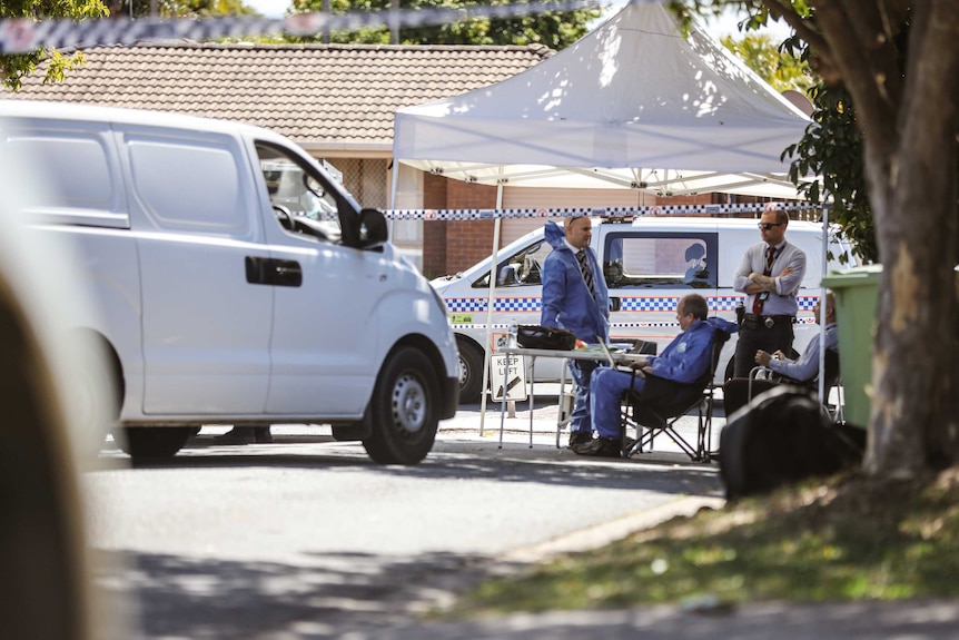 Detectives talk under a tent at a crime scene near police vans.
