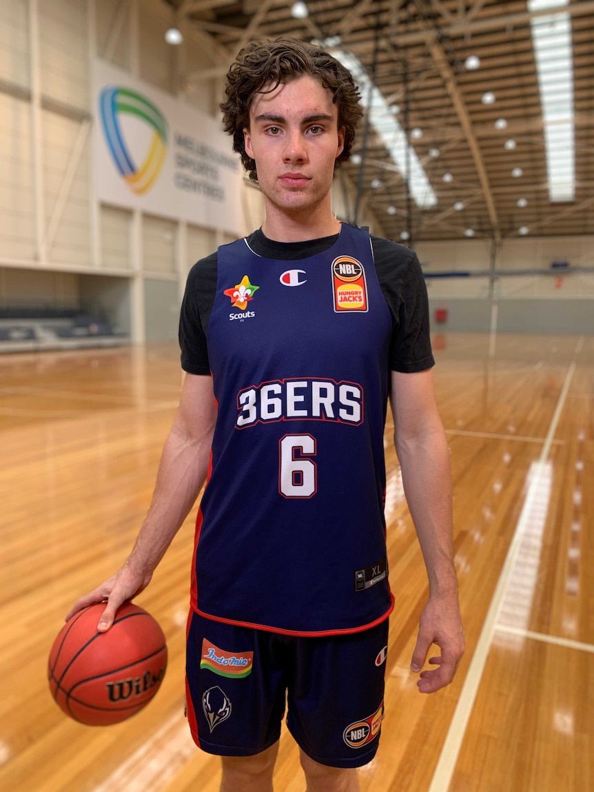 NBL player Josh Giddey holding a basketball in one hand at a gym in Adelaide 36ers gear.