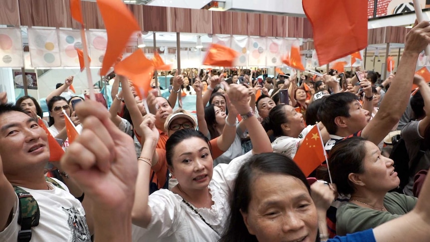 At least a hundred people wave Chinese flags as they look up during a packed demonstration at a mall.