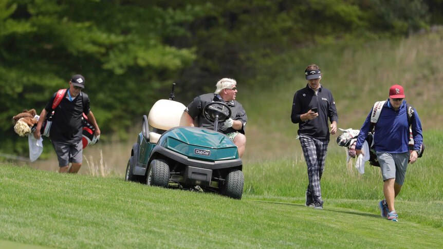 A golfer in a golf cart talks to another golfer as they go down a fairway.