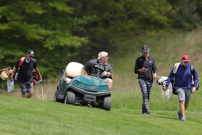 A golfer in a golf cart talks to another golfer as they go down a fairway.