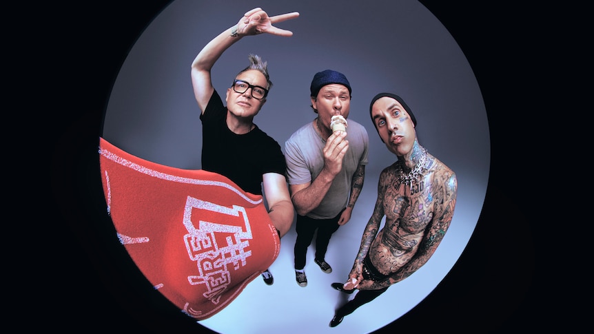 Three members of Blink-182 shot through a fisheye lens. Travis Barker is shirtless, Mark Hoppus holds up the peace sign