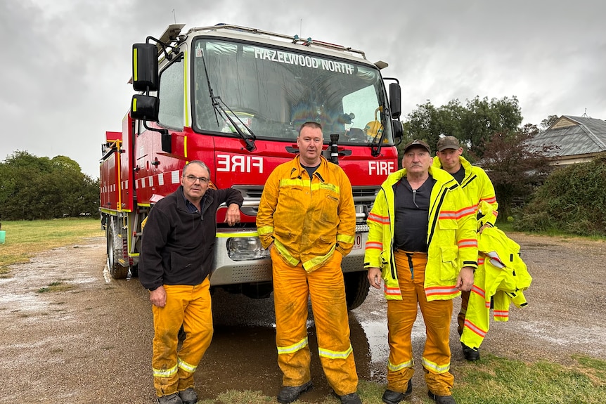 Four firefighters standing in front of a fire truck.