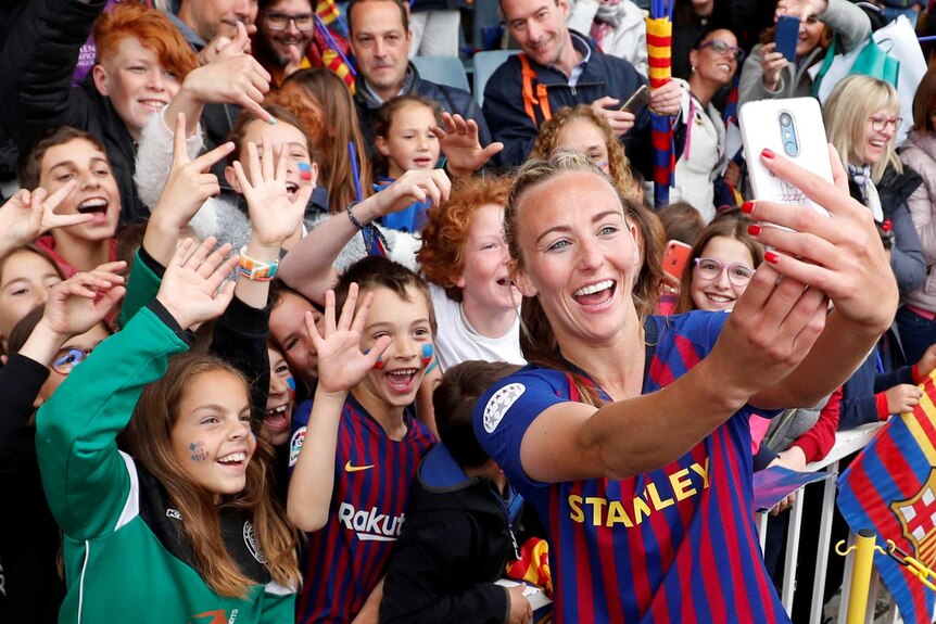 A female soccer player takes a selfie in front of a crowd.