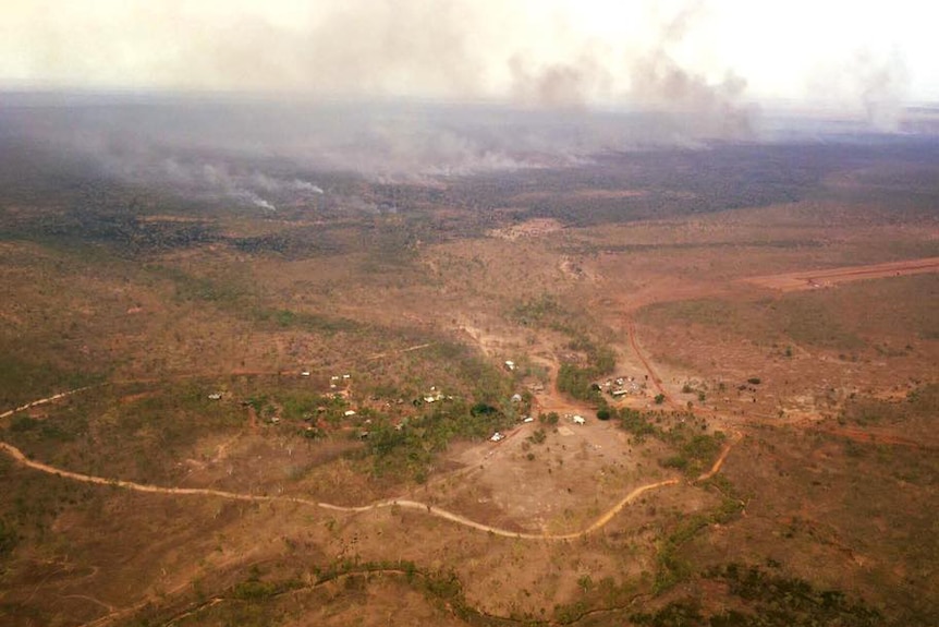 An aerial shot of a bushfire burning near a remote community with smoke rising into the sky.