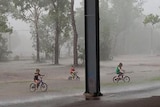 Children riding bikes in Top End rain make for the safety of a covered area, at Freds Pass, near Darwin.