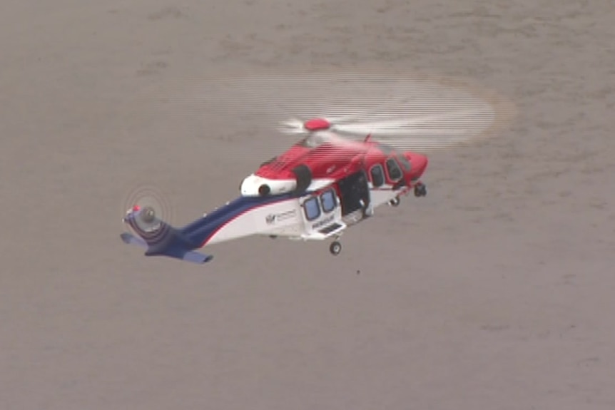 A rescue helicopter flies over a grey body of water.