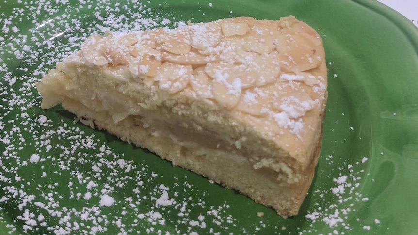 A slice of apple shortcake with a basket of apples in the background.