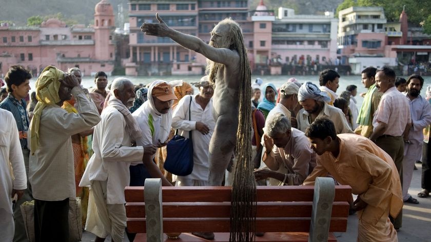 A Hindu holy man stands on a bench as devotees pay their respects on the banks of river Ganges during the Kumbh Mela festival on April 13, 2010 in Haridwar, India.