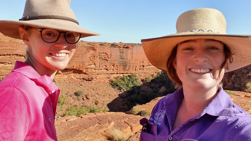 Two women wearing wide-brimmed hats smile and take a selfie at scenic spot in a desert.