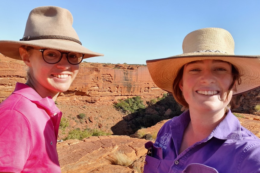 Two women wearing wide-brimmed hats smile and take a selfie at scenic spot in a desert.