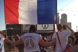 A woman holds a French flag and wears a shirt with the #PeaceForParis symbol on the back