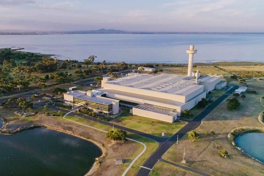 A drone shot of the Australian Animal Health Laboratory, a bit white building surrounded by water and bushland.