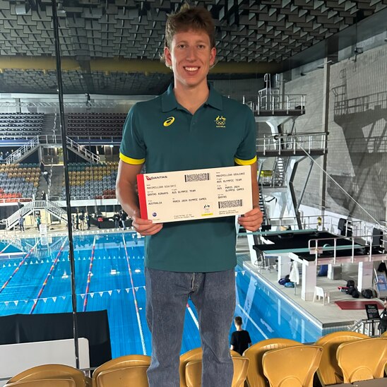 Max Giuliani is a tall, blond young man, standing in front of a swimming pool holding a ticket to the Paris Olympic games.
