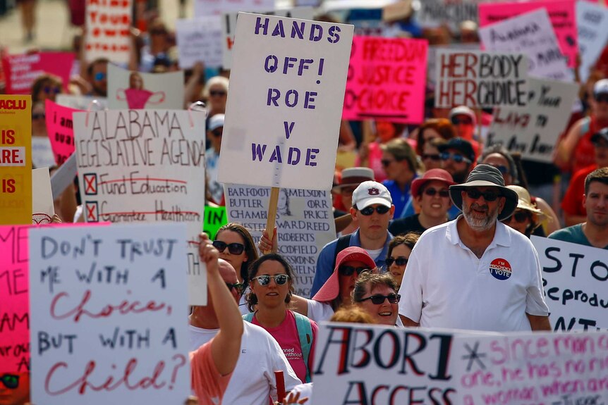Protesters marching with signs that read "Hands off Roe v Wade" and "Don't trust me with a choice, but with a child?"