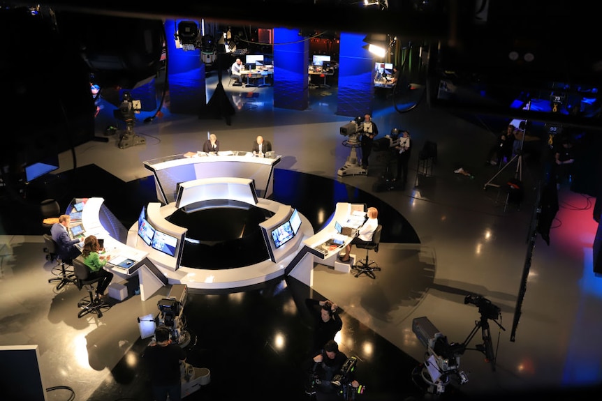 Aerial shot of presenters sitting on election set in studio, cameras and support staff on computers in background.