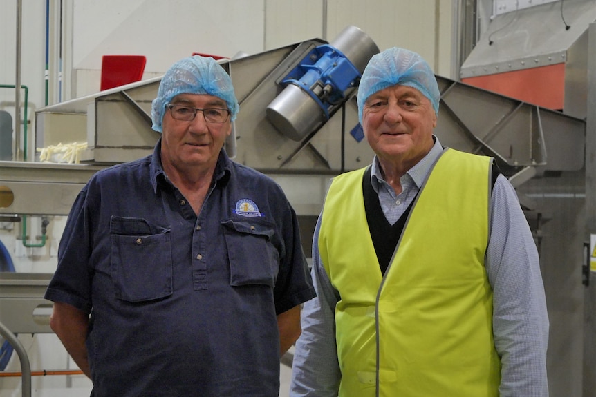 Two men stand in hi-vis gear and hair nets in a food processing plant.