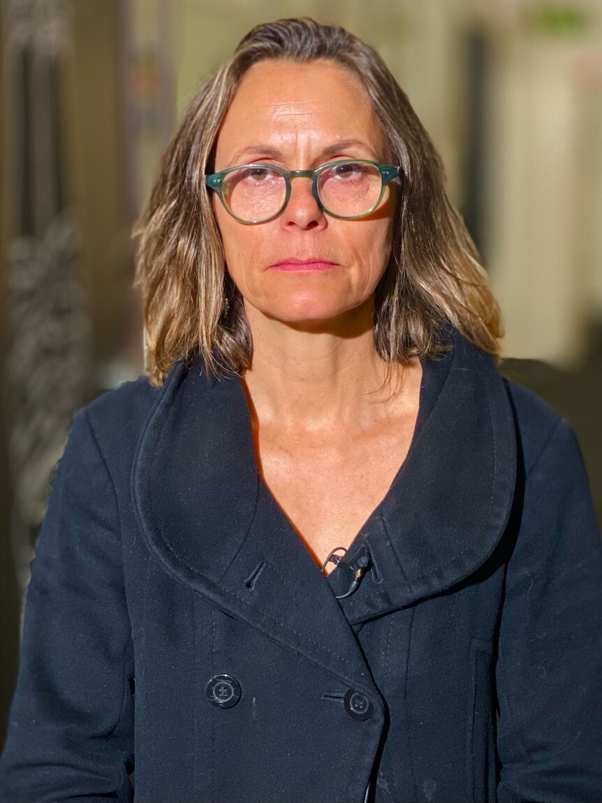 A woman with glasses and a sombre expression.