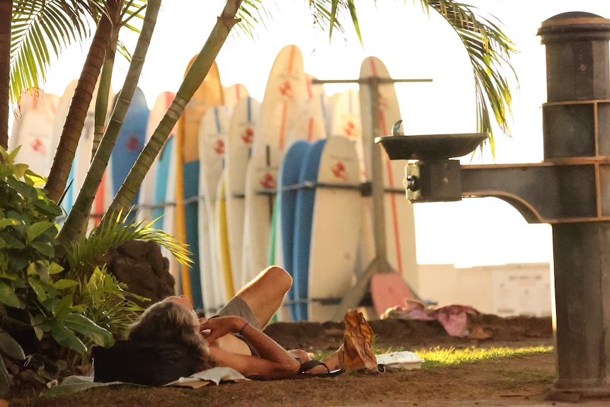 A homeless man reclines behind surfboards on Waikiki Beach, Hawaii