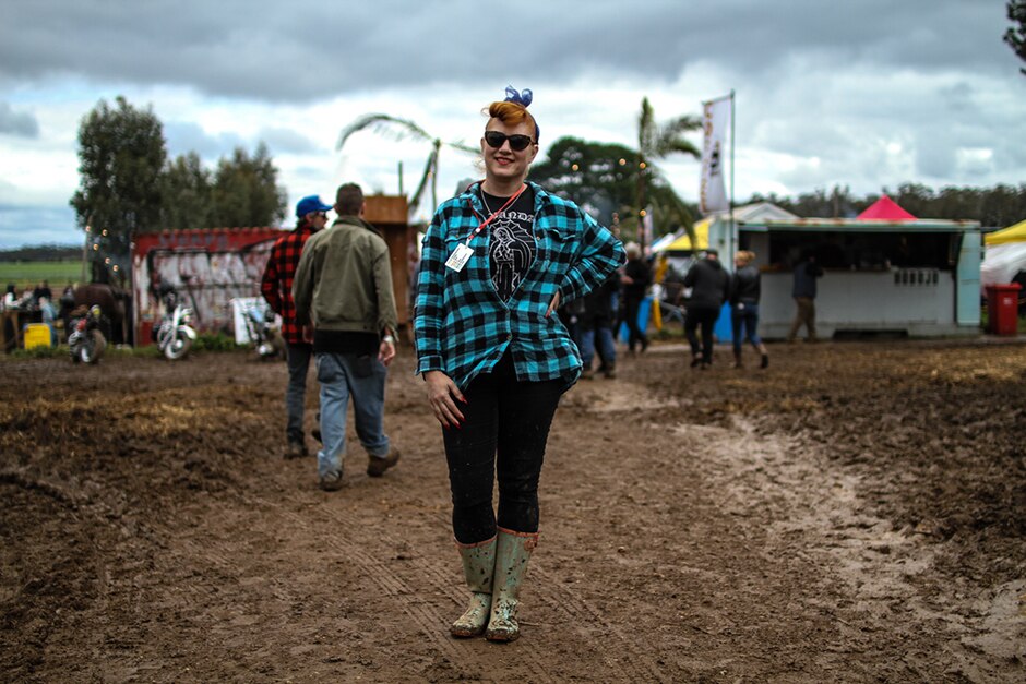 A woman in sunglasses and blue-and-black checked flannel shirt stands on a muddy track.