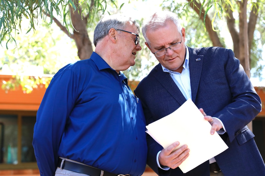 Un hombre con una camisa azul habla con el primer ministro Scott Morrison en Alice Springs.  Morrison tiene papeles en la mano.