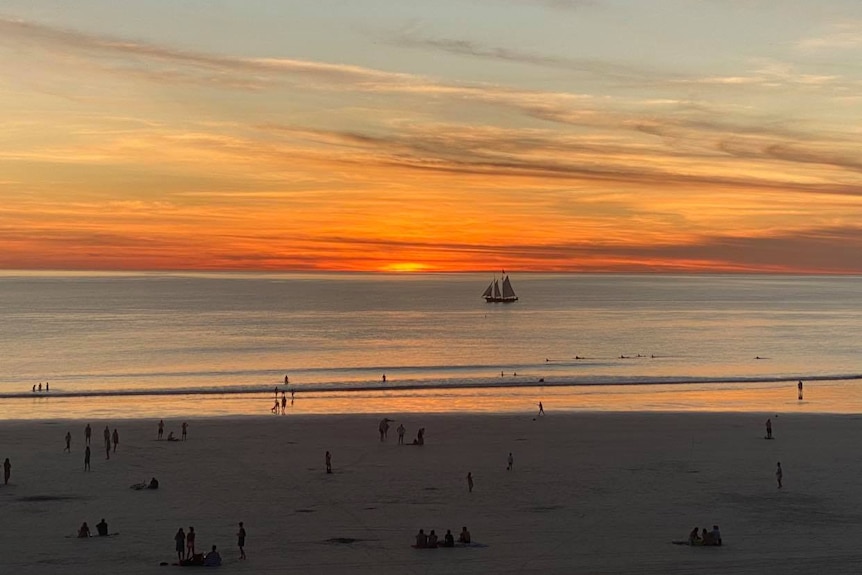 Image of tourists gathered on an overlook near a beach taking photos of the sunset.