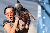 A woman celebrates, holding her small dog aloft after winning the World's Ugliest Dog Contest