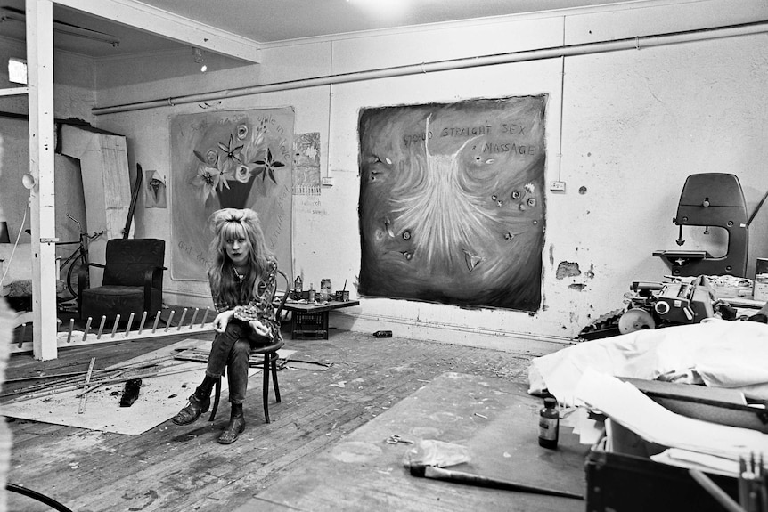 A black and white photo from the 1980s of a woman sitting on a chair alone in art studio