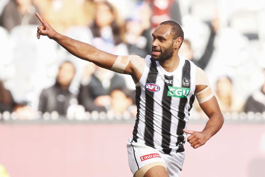 Travis Varcoe points to his right while looking in the same direction. He is smiling.