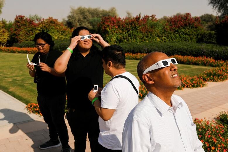 Four people standing outside wearing special purpose eclipse glasses, looking up at the sky