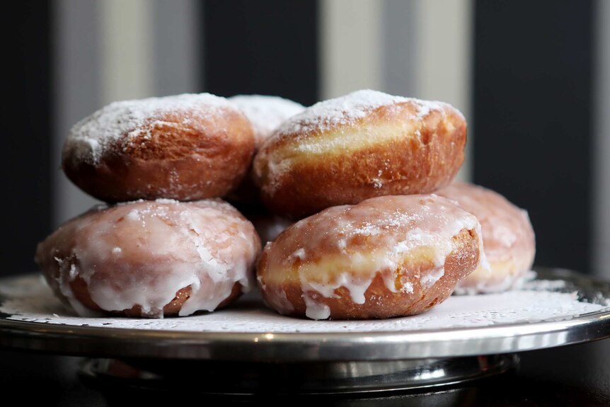 A stainless steel cake stand with a pile of pączki, traditional Polish donuts, with glaze and icing sugar.