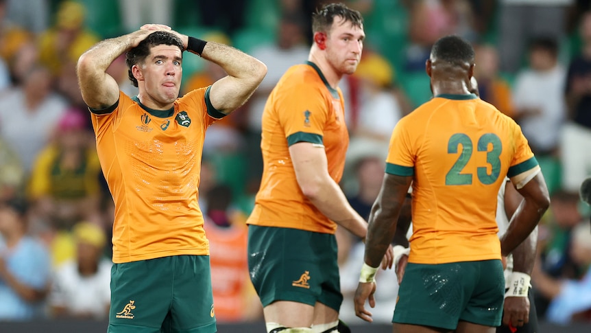 Three Wallabies players stand on the ground after the 2023 Rugby World Cup loss to Fiji.