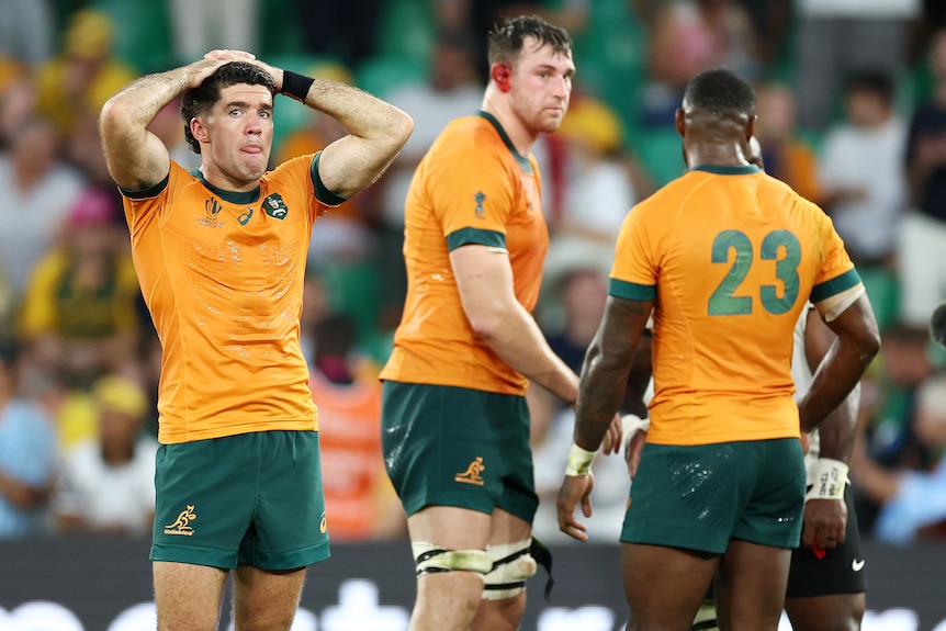 Three Wallabies players stand on the ground after the 2023 Rugby World Cup loss to Fiji.