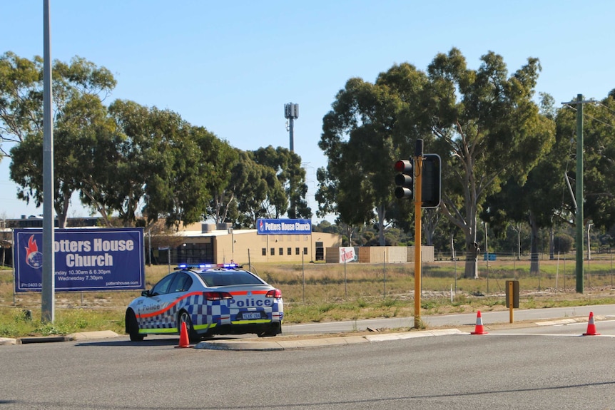 A police car and witches hats block Beechboro Road North, near the entrance to the Potter House Church.