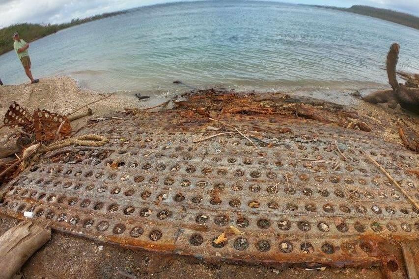 The remains of a seaplane launchpad are seen laying on the beach under clear water.
