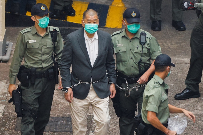 Apple Daily founder Jimmy Lai is led away to a prison van in handcuffs after being charged