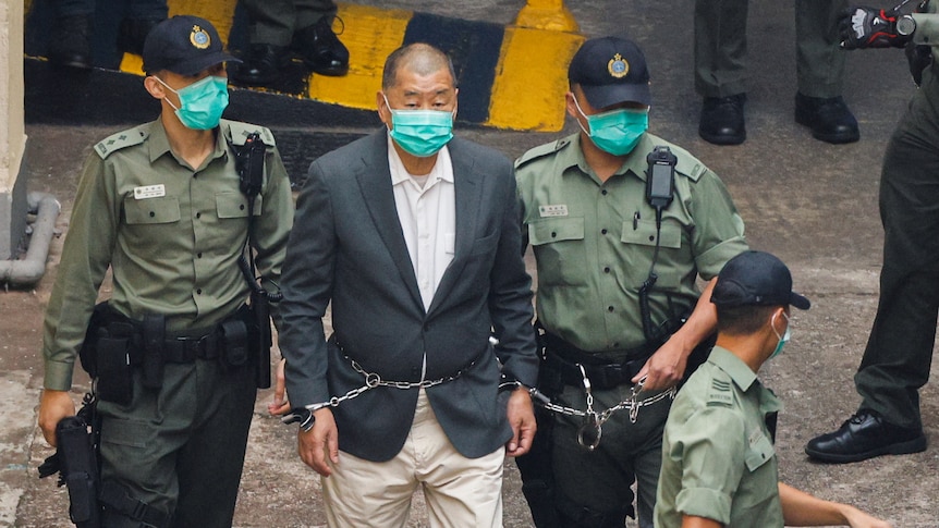 Apple Daily founder Jimmy Lai is led away to a prison van in handcuffs after being charged