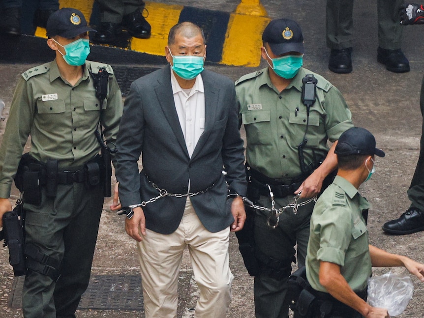 Apple Daily founder Jimmy Lai is led away to a prison van in handcuffs after being charged