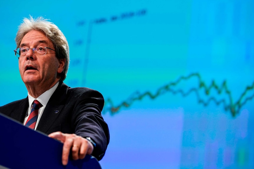 A man speaks at a podium with a graph projected in the background.