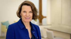 Sue Shilbury wearing blue jacket stands in meeting room with table and chairs in background