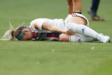 Footballer Ellie Carpenter lying on the ground, holding her right knee, face in the turn in pain, after suffering an ACL injury
