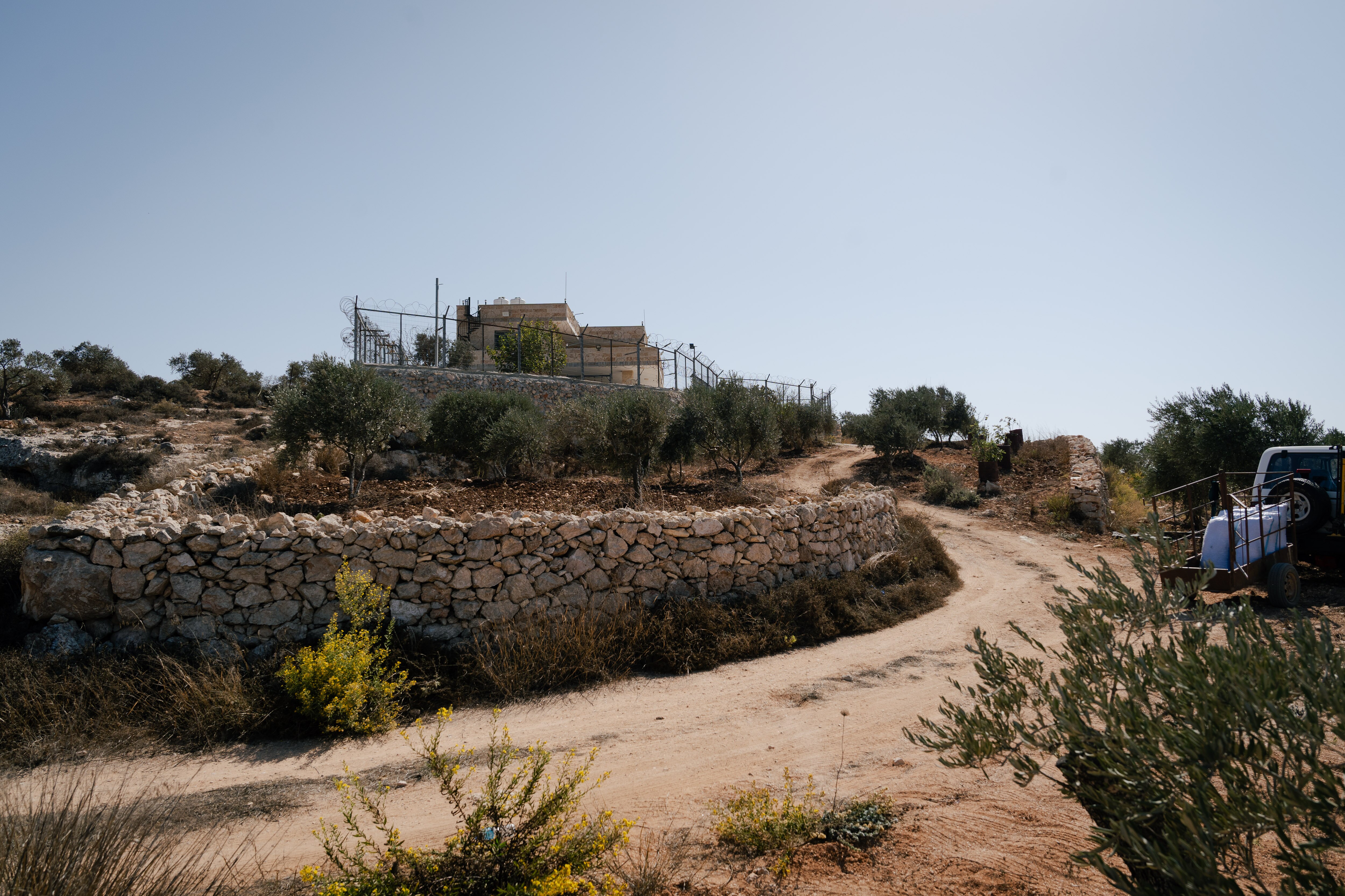 A house on a small hill surrounded by olive trees and dirt roads