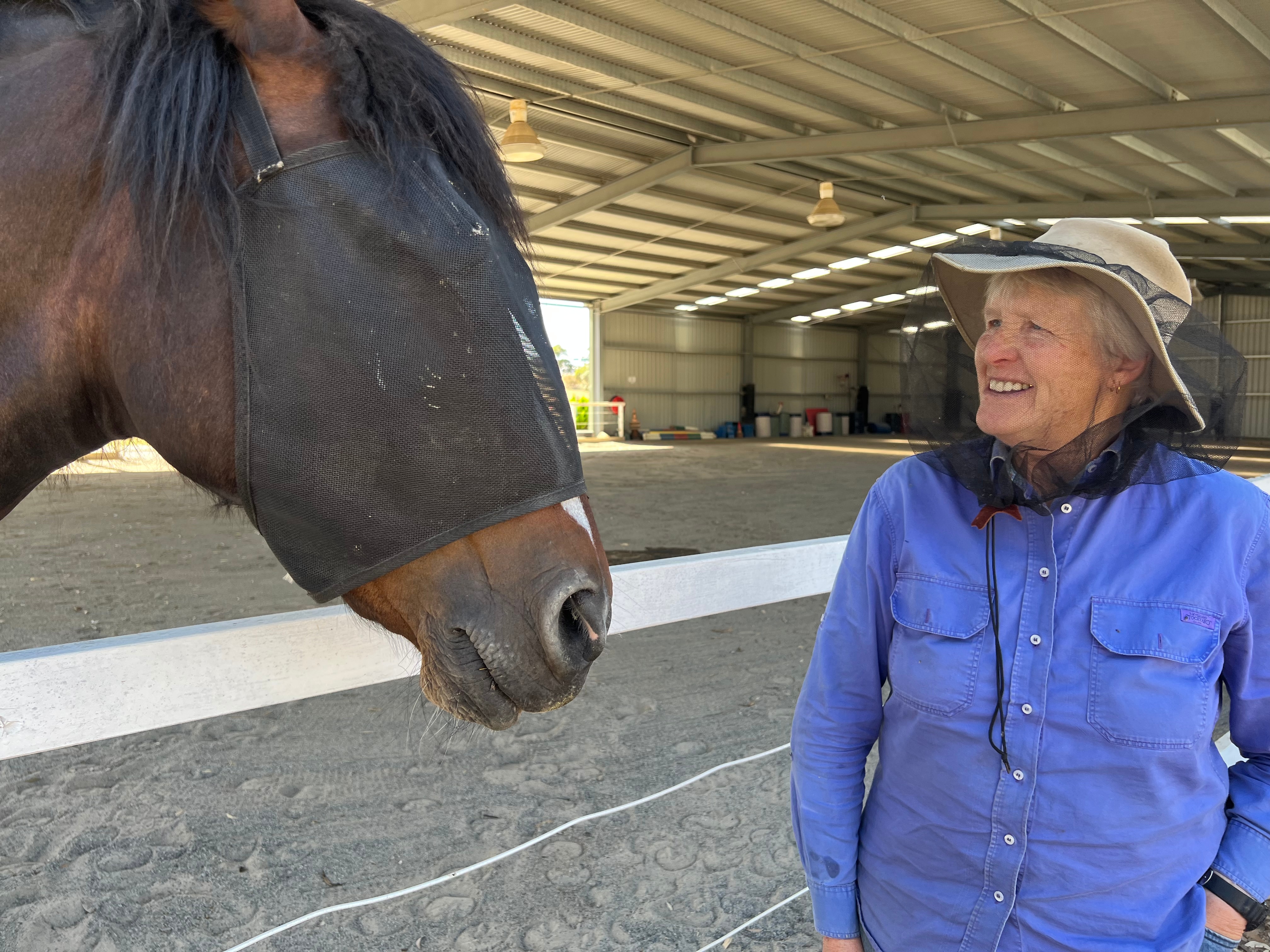 Uma mulher com um chapéu de mosquiteiro fica ao lado de um cavalo em um picadeiro