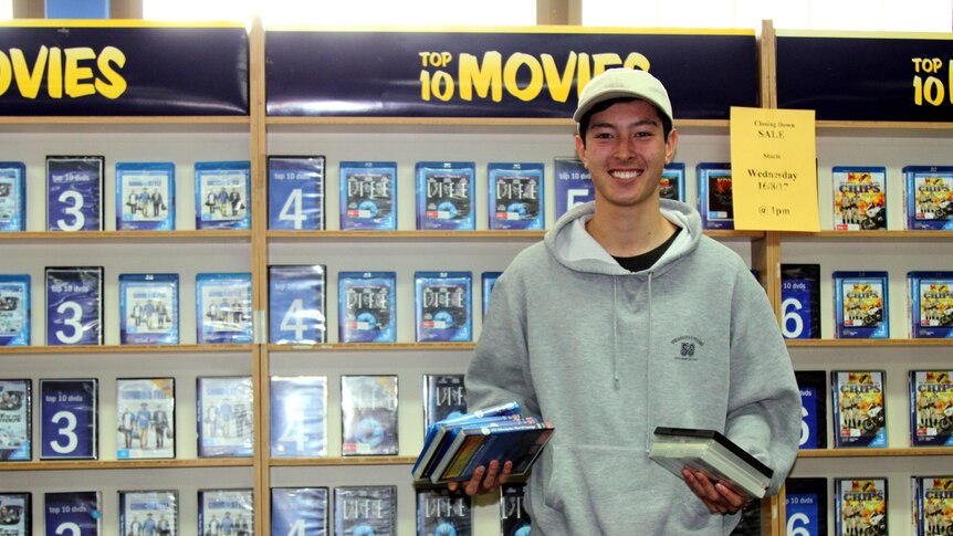 Blockbuster employee stands in front of DVD shelf