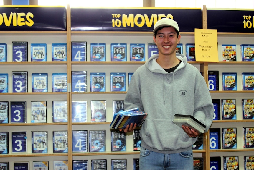 Blockbuster employee stands in front of DVD shelf