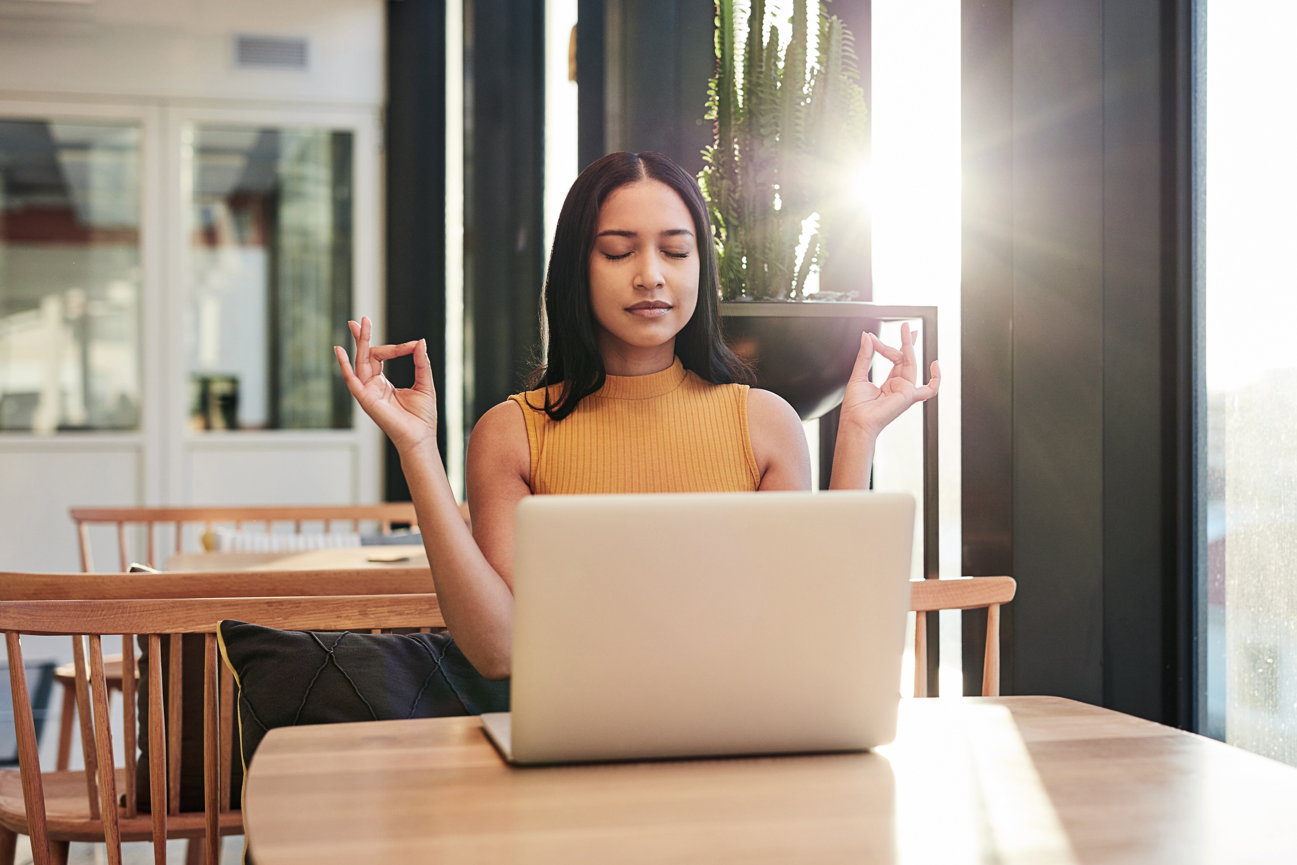 Woman sitting behind her laptop with hands held in a yoga pose with fingers touching thumbs