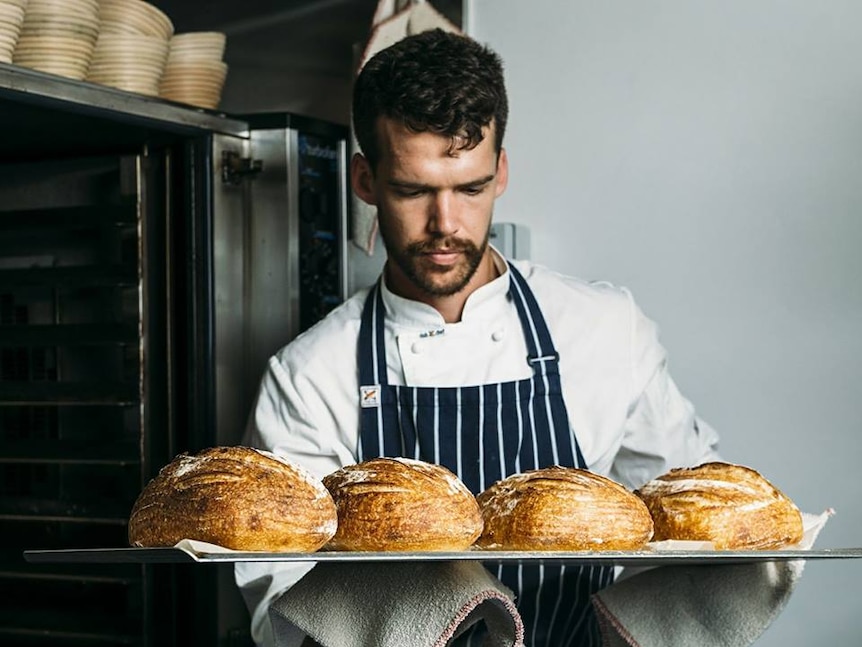 Pastry chef Will Jane inspects four sourdough loaves in his kitchen.