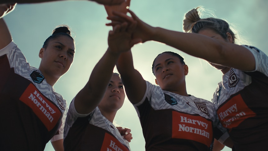 Four Queensland Maroons women's players in a huddle, with their hands in the middle