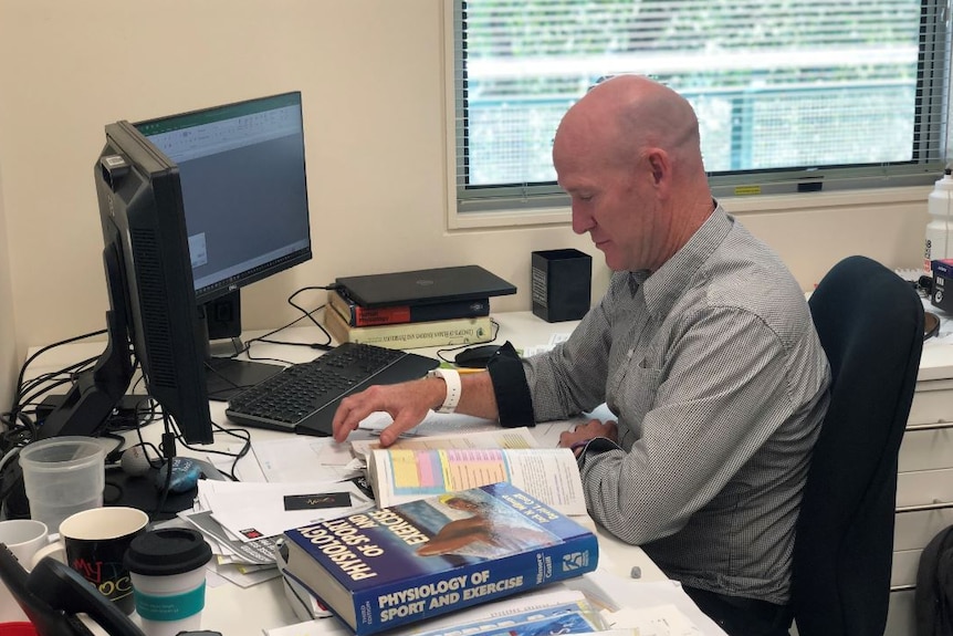 Dr Vince Kelly sits at his desk with a computer in front of him and a textbook next to him