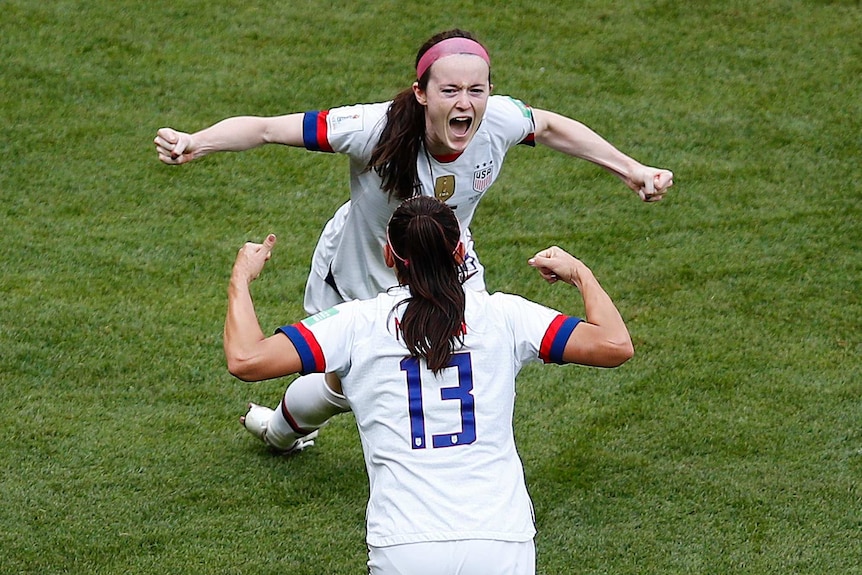 Rose Lavelle screams and holds her arms wide as she runs towards Alex Morgan, who is facing away from the camera in same pose